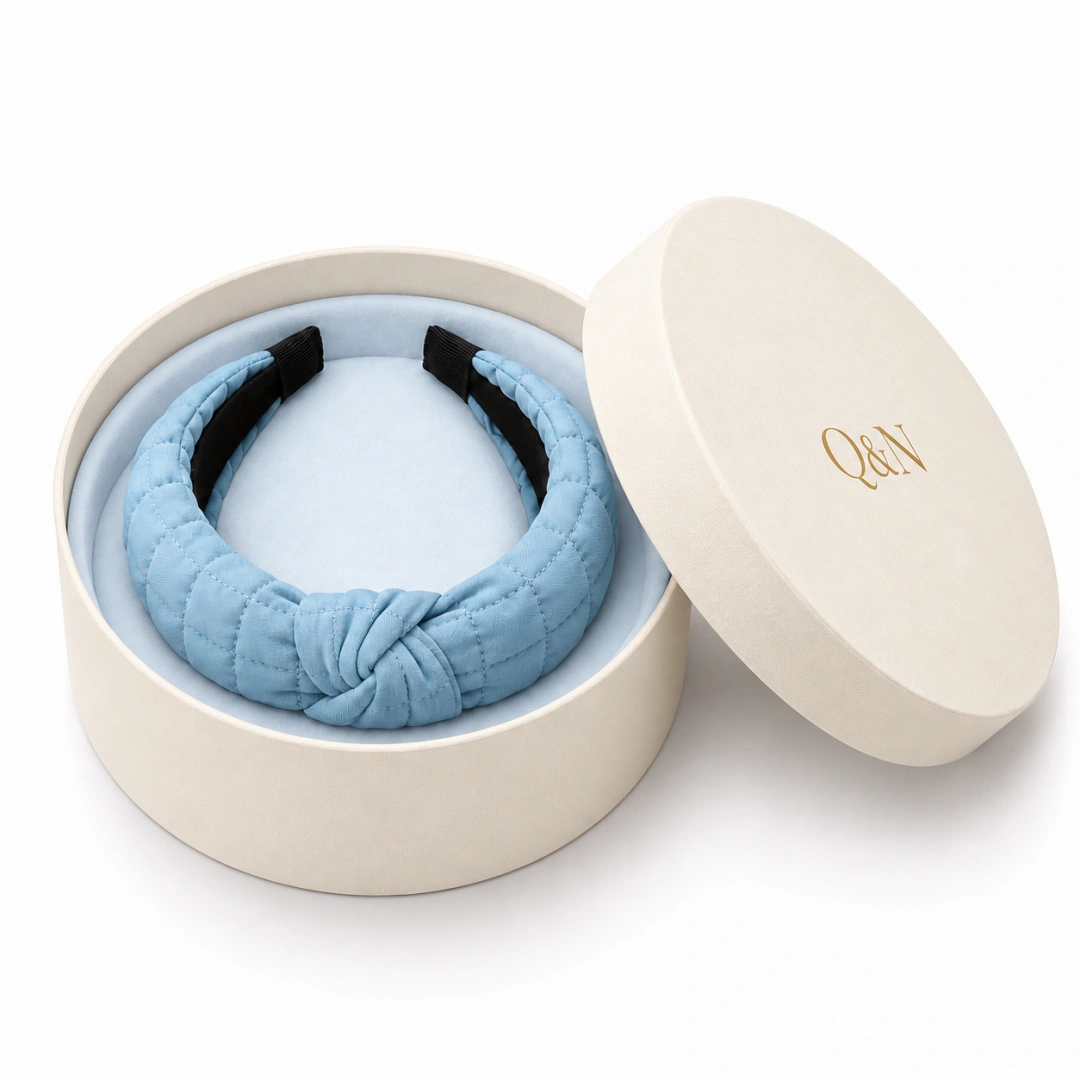 Blue knotted headband in an ivory round gift box with a branded lid